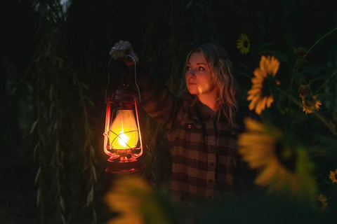 Person holding a glowing 12 Inch Hurricane Lantern With Durable Red Finish For Camping And Emergencies outdoors at night.