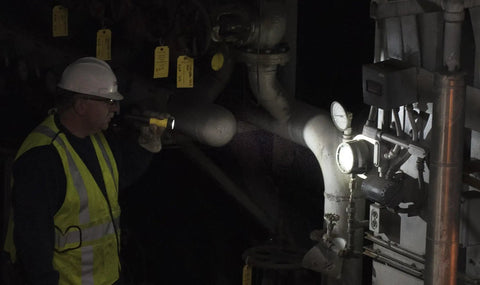 Worker using PolyStinger LED Flashlight With DC Charger And Piggyback Holder, Yellow, 485 Lumens, inspecting industrial pipes.