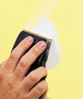 Applying spackling on yellow wall, smoothing surface for interior and exterior use with dry time indicator ensuring crack resistance.