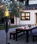 Outdoor scene featuring Six Pack 59 Inch Outdoor Tiki Torches for Patio and Garden with Citronella, Metal Torch, and a dining setup.