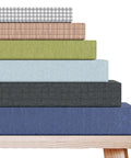 Assorted custom bench cushions with fabric color and size options non slip waterproof high density foam piping trim stacked on a wooden bench