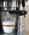Top Tier Stainless Steel Espresso Machine With Reliable 19 Bar Italian Pump And Quick Ground Or ESE Pod Brewing Featuring Precise Temp Control And Zero Frustration Pre Brew For Killer Daily Coffee Routines brewing espresso into a glass mug with milk foam.