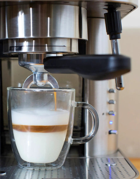Top Tier Stainless Steel Espresso Machine With Reliable 19 Bar Italian Pump And Quick Ground Or ESE Pod Brewing Featuring Precise Temp Control And Zero Frustration Pre Brew For Killer Daily Coffee Routines brewing espresso into a glass mug with milk foam.