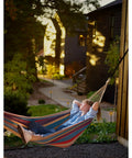Person relaxing in hammock in garden with Outdoor Solar Flickering Torch Lights 8 Pack Waterproof Patio Tiki Lamps installed along pathway.