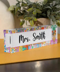 Customizable Teacher Desk Name Plate In 12 Designs And 9 Fonts, Available In 2 Sizes, Acrylic Office Name Plate Gift For Teachers, Personalize With Name And Title For Any Classroom with decorative border, displaying 'Mrs. Smith'. Acrylic material on desk.