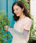 Heavy Duty Cut Resistant Arm Sleeves With Thumb Hole Tough As Nails Forearm Guards Designed For Welding And Auto Repair worn by a woman in a garden.