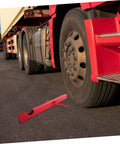 Red Manual Strap Winder For Trucks placed on asphalt next to a truck tire, Hand Crank Cargo Belt Winder Tool ready for use
