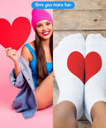 Woman holding red heart shape with feet in white socks featuring heart design on wooden floor