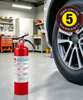 Grab And Dash Two Point Five Lb Multi Purpose Fire Extinguisher Legit Heavy Duty Kick For Home Workshop next to a car tire in a garage.