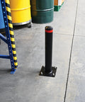 Badass 24 Inch Steel Garage Safety Bollard Wall Defender Pipe Guard With Pre Drilled Mounting Holes Matte Black Finish standing in a warehouse.