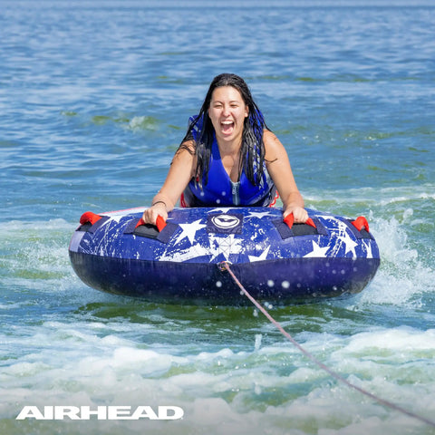 Airhead Stars And Stripes Towable Tube For 1 Rider Boating And Water Sports Made In The USA Heavy Duty Full Nylon Cover Patented Speed Safety Valve For Easy Inflation And Deflation Foam Padded Handles, front view on water