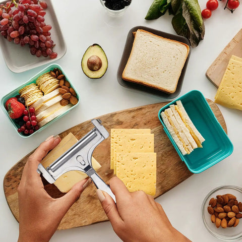 Adjustable Cheese Slicer With Four Replaceable Stainless Wires Heavy Duty Aluminum Alloy Handheld Cheese Cutter For Block And Sharp Cheeses slicing cheese on a wooden board with snacks around.