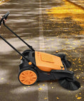 Walk Behind Floor Sweeper Featuring An Extra Wide 41 Inch Triple Brush Design, cleaning leaves off a concrete path.