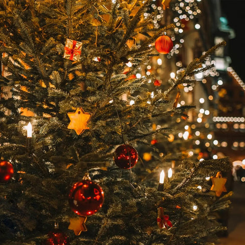 Decorated Christmas tree with lights and ornaments featuring red baubles and star-shaped decorations, glowing in a festive setting.
