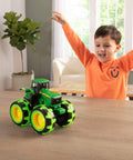 John Deere Monster Treads Lightning Wheels Monster Truck Toy With Motion Activated Lights, Oversized Monster Truck Wheels, Durable Build For Rollover Fun, Realistic Tractor Look For Ages 3 Years And Up on table with child in background