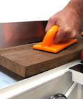 Hand using orange push block from Heavy Duty Five Piece Woodworking Safety Kit to secure wood on a jointer table.