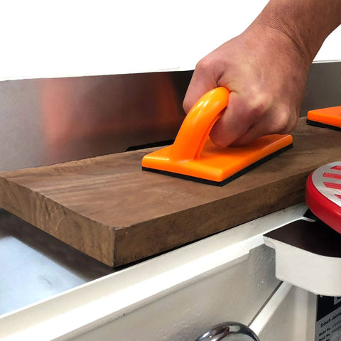 Hand using orange push block from Heavy Duty Five Piece Woodworking Safety Kit to secure wood on a jointer table.