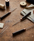 Top Shelf 3 Piece Scratch Awl Tool Set Featuring Sick Ergonomic Wood Grips And Razor Sharp Tips for Leather Crafting on wooden table.