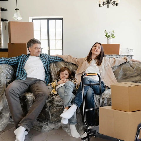 Folding hand truck with black steel frame and orange handle, placed beside packed boxes in a living room