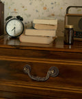 Six Pack Antique Brass Drawer Pulls With Four And Three Quarters Inch Hole Centers on wooden cabinet scene with books and clock