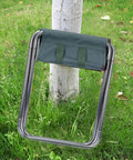 Portable Oxford Cloth Folding Stool With Lightweight Aluminum Frame For Outdoor Camping And Picnics Easy Foldable Chair For Fishing And BBQs Compact Sturdy And Comfortable Dark Green Seat beside a tree