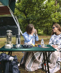 Two campers sitting by Ultra Lightweight Aluminum Folding Camping Table With Adjustable Legs Portable Beach And Picnic Table outdoors