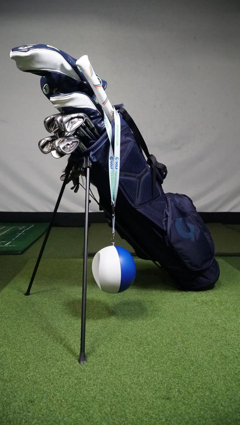 Compression Ball Golf Swing Trainer For Perfect Impact And Forearm Connection next to golf bag on indoor turf floor