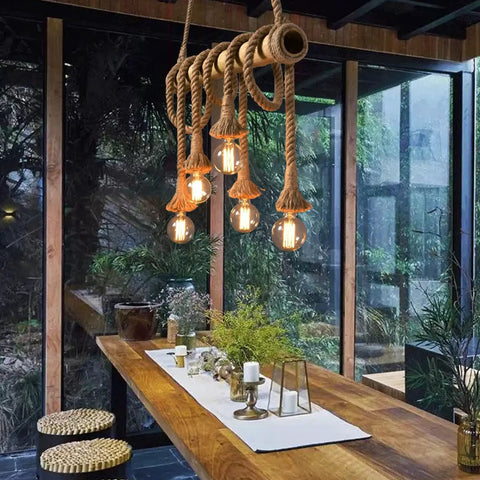 Six Heads Hemp Rope Pendant Light With Vintage Bamboo Chandeliers Fixture hanging over rustic dining table with greenery.