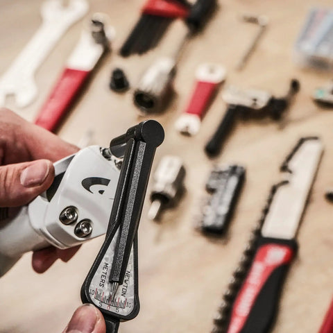 Close-up of a torque wrench from 18 Piece Bike Repair Tool Kit Set With Torque Wrench For Mountain And Road Bikes A Must Have For Quick Maintenance Includes Chain Rivet Extractor Pedal Wrench 15mm Spanner Hex Keys Screwdrivers And Half Inch Drive Adapter surrounded by various tools on a wooden surface.
