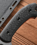 Close-up of carbon fiber handle on Rugged Fixed Blade Knife With DC53 DLC Coated Nine Point Eight Four Inch Blade Carbon Fiber Handle Full Tang Build Includes Sheath Built For Outdoor Camping Hunting And Tough As Nails Work Premium Steel Edge For Heavy Use against a wood background.