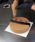 Person wearing nitrile disposable gloves extra large black powder free industrial grade decorating a round cake with frosting.