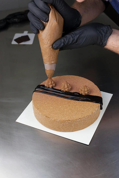 Person wearing nitrile disposable gloves extra large black powder free industrial grade decorating a round cake with frosting.