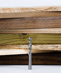 Router bit, spiral downcut with 1/4-inch shank, solid carbide, standing upright in front of stacked wood boards.
