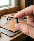 Close-up of Top Shelf Black Chicago Screws And Binding Post Tools For Leather Crafting And Scrapbook Binding M4 X 8mm Carbon Steel Fasteners held between fingers.