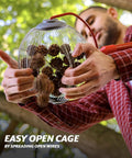 Person demonstrating the open cage feature of the Back Saving Nut Gatherer Roller For Pecans Hickory Nuts Golf Balls And More Yard Picker Upper With Durable Steel Cage And Ergonomic Handle No Bending Needed Easy Roll Action Newest Model.