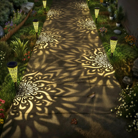 Pathway illuminated by Six Pack Solar Outdoor Garden Lights With Mandala Pattern, Warm Amber Glow, Waterproof, in black.