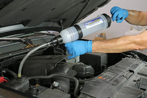Side view of Mityvac 1.5 L fluid evacuator in use under car hood with blue-gloved hands and attached hose.
