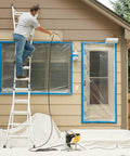 Professional HEA Airless Paint Sprayer in use on exterior house, person on ladder applying paint to wall, protective covering in place.