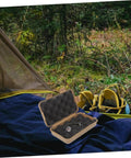 Tough Mud Color Outdoor Storage Box Shockproof All Purpose Case For Camping Hiking And Field Gear open next to camping gear in forest.