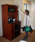 A woman using a Lightweight Portable Canister Vacuum delivering beefy suction in green and black to clean above a microwave.