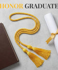 67 Inch Gold Graduation Honor Cord With Tassels next to diploma and book on gray background