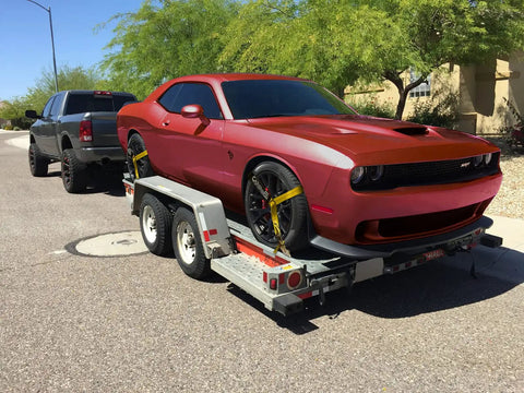Red car secured on trailer using Heavy Duty Wheel Tie Down Straps 4 Pack For Tow And Hauling, 2 Inch Wide With Double J Hooks
