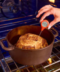 Person using ThermoPop 2 Instant Read Thermometer in Cayenne Red to measure bread temperature in a dark pot inside oven.