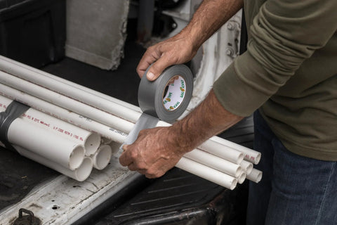 Side view of hands applying gray Duck Brand duct tape to white PVC pipes (1-pack, 60 yd).