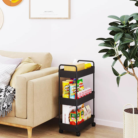 Three Tier Rolling Storage Cart With Adjustable Shelves, Mobile Utility Organizer On Wheels For Kitchen, Bath, And Laundry, Narrow Space Saver In Black Finish next to a couch holding snacks.