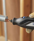 Dremel rotary tool cutting a metal pipe with a brown grinding bit; black body and blue switch, gloved hand