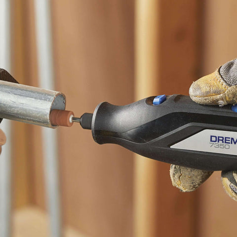 Dremel rotary tool cutting a metal pipe with a brown grinding bit; black body and blue switch, gloved hand