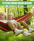 Two children relaxing in a striped hammock supported by two detachable wood hammock spreader bars in a sunny forest setting.