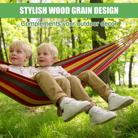 Two children relaxing in a striped hammock supported by two detachable wood hammock spreader bars in a sunny forest setting.