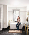 Bathroom with gold fixtures and a woman seated on a bathtub